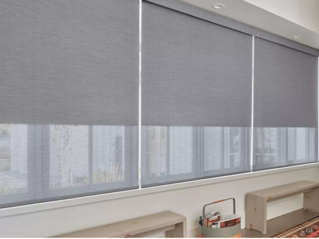 Motorized roller shades hang from a window, with a sleek design and smooth texture.